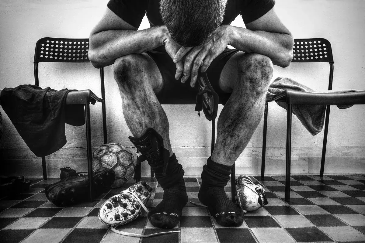 Black-and-white photo of an exhausted soccer player sitting in a locker room with his head down.