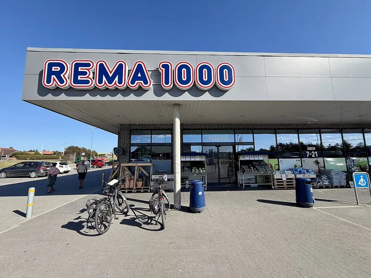 Exterior of a REMA 1000 grocery store with bicycles and shoppers outside.