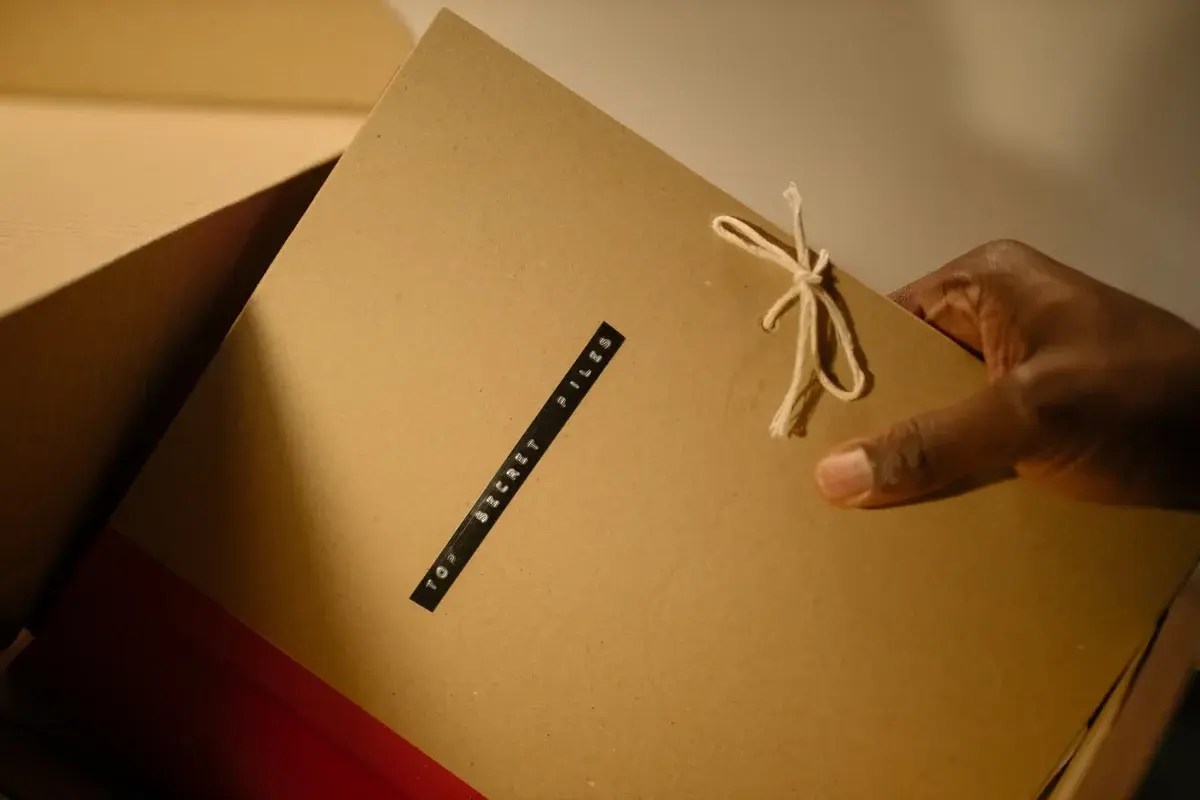 A hand holds a tan folder tied with string and labeled top secret files.