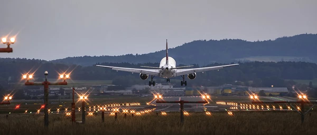 A Swiss airplane approaching landing at Zurich Airport at dusk with runway lights glowing.