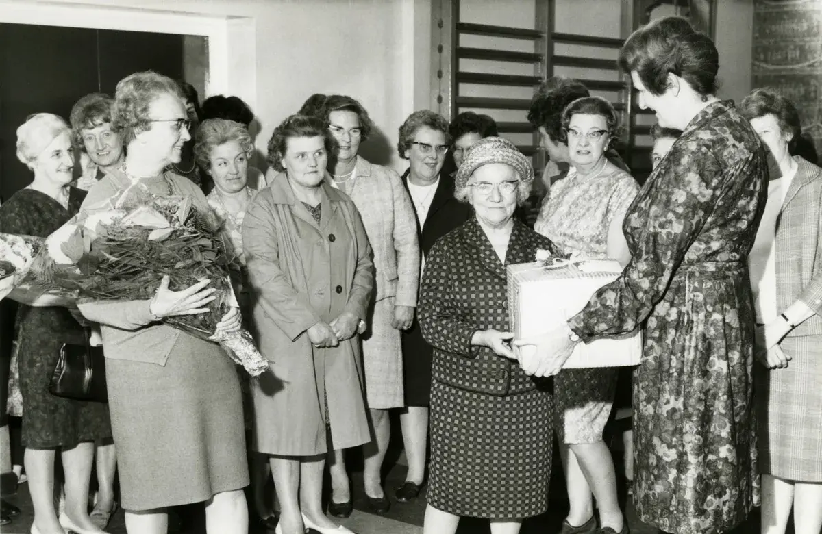 Older women at a formal ceremony receiving flowers and gifts.