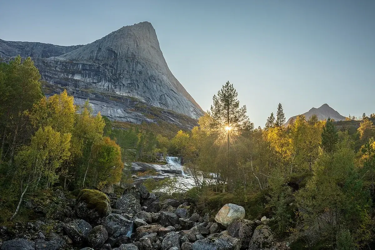 Mountain landscape with a river, waterfall, autumn trees, and sunlight in Narvik, Norway.