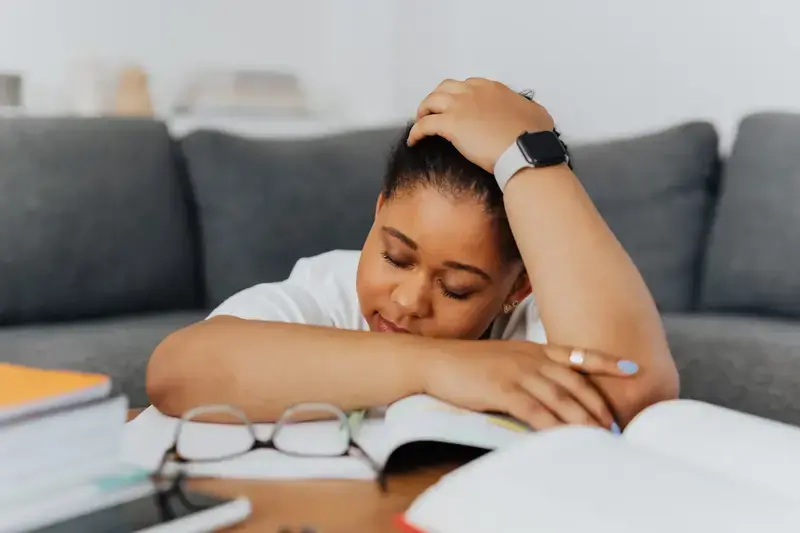 Tired woman resting on books while studying