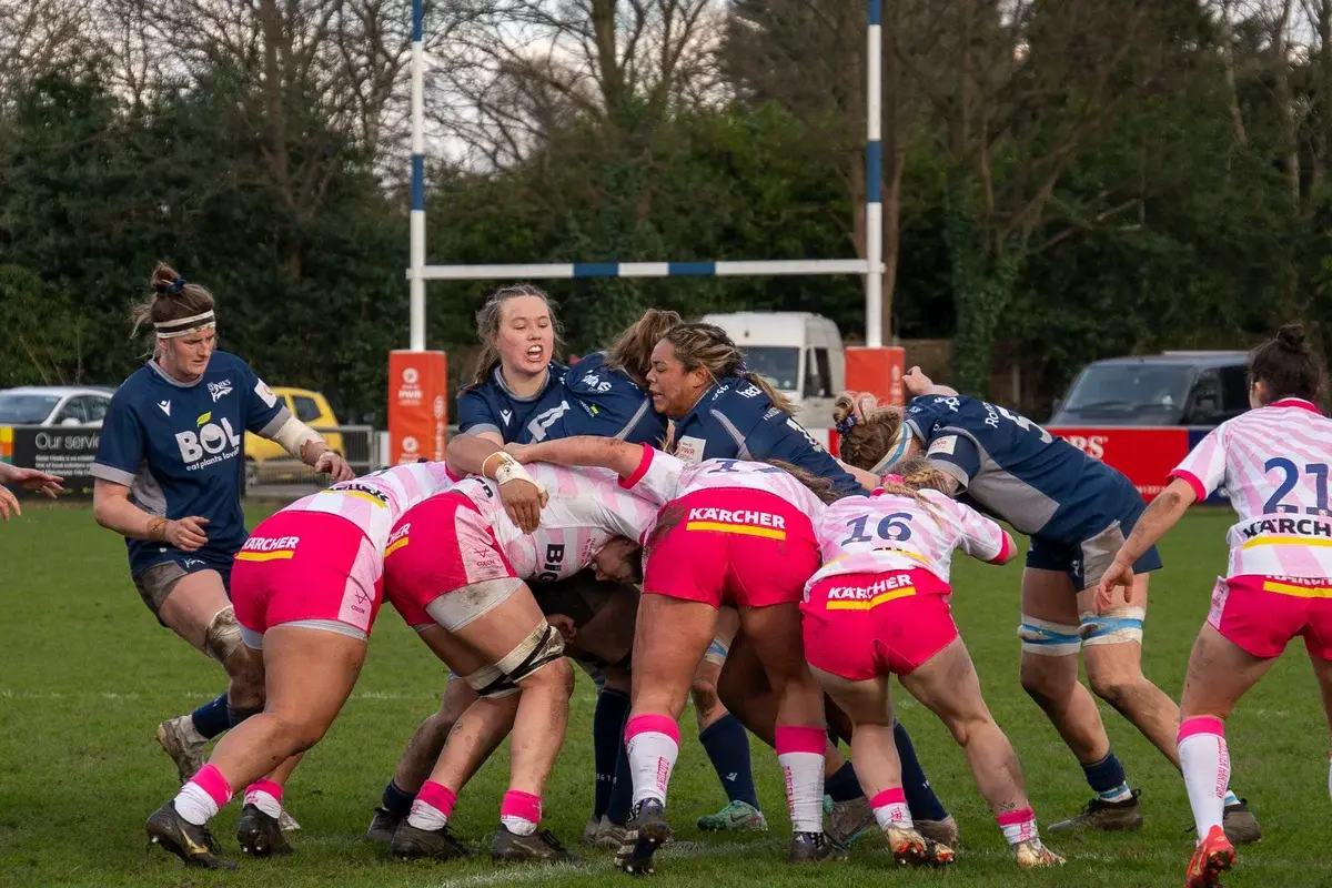 Women playing a rugby match on a grass field.