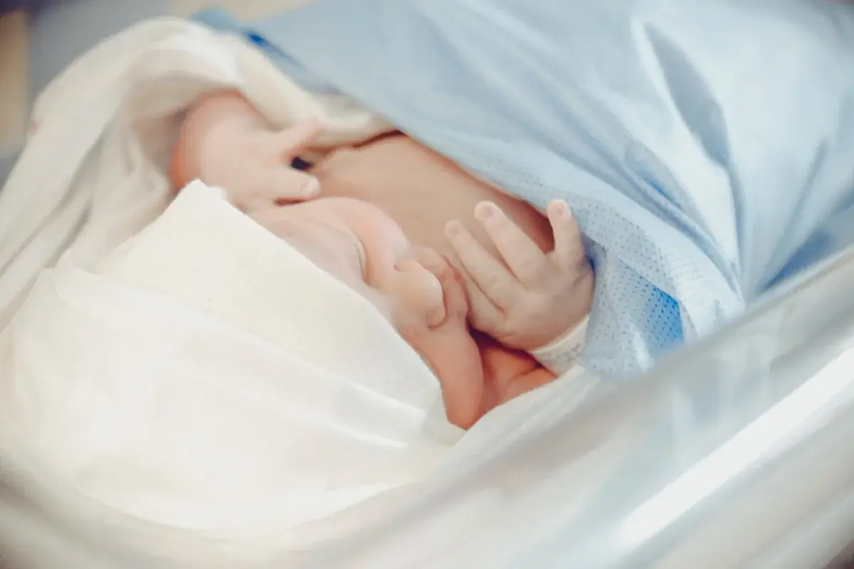 Newborn baby sleeping in a hospital bed wrapped in a blue blanket.
