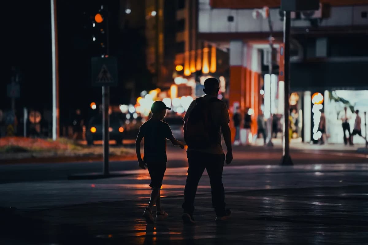 Silhouetted father and son walking through a city at night.