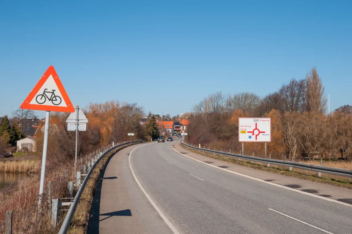 A quiet rural road in Denmark with road signs and trees.