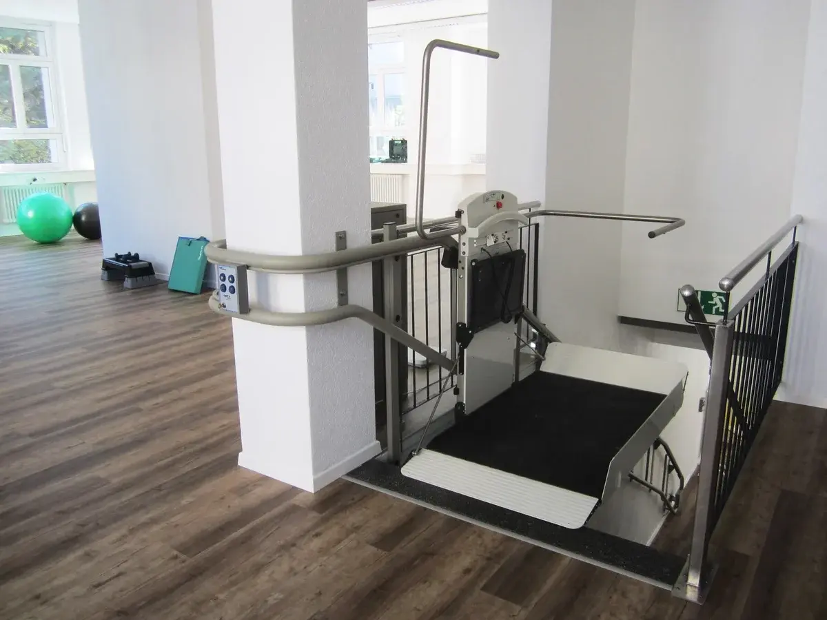 An indoor platform lift in a bright rehab room with exercise equipment.