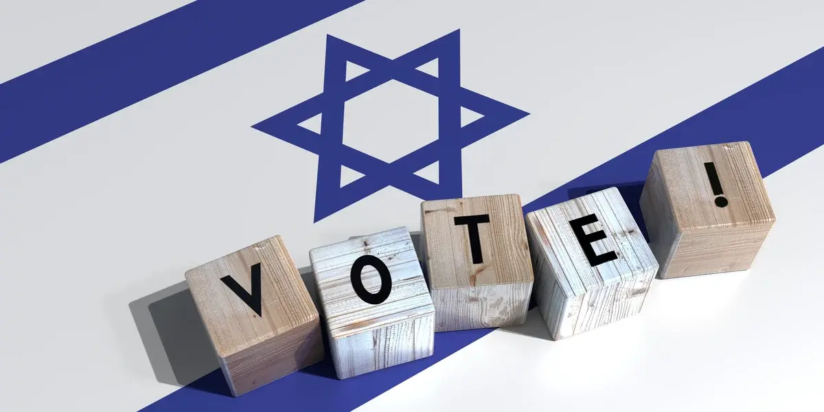 Wooden blocks spelling vote in front of the Israeli flag.