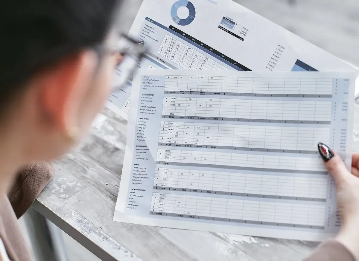 A woman examines printed financial spreadsheets with charts and graphs.