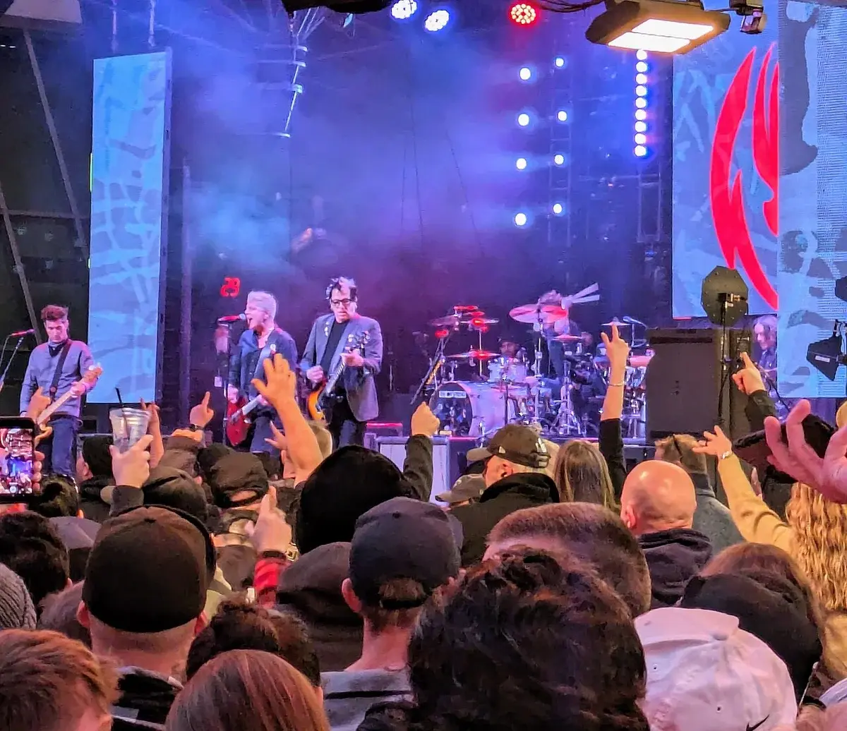 A rock band performing on stage in front of a crowd at an outdoor concert.