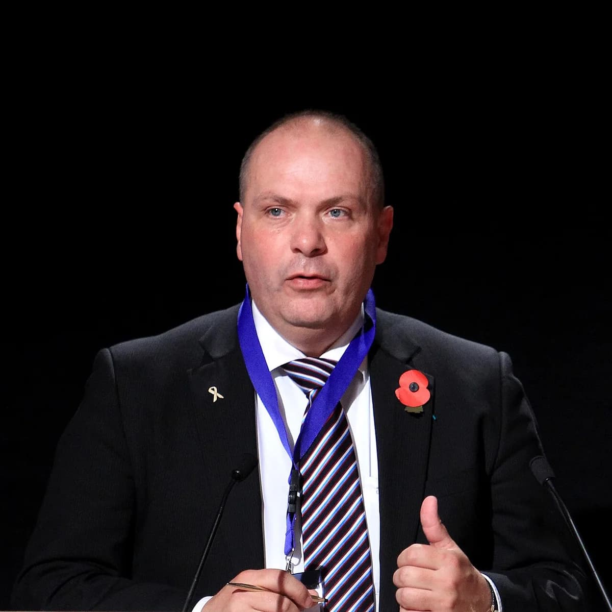 A man in a suit and tie speaking at a podium with microphones.