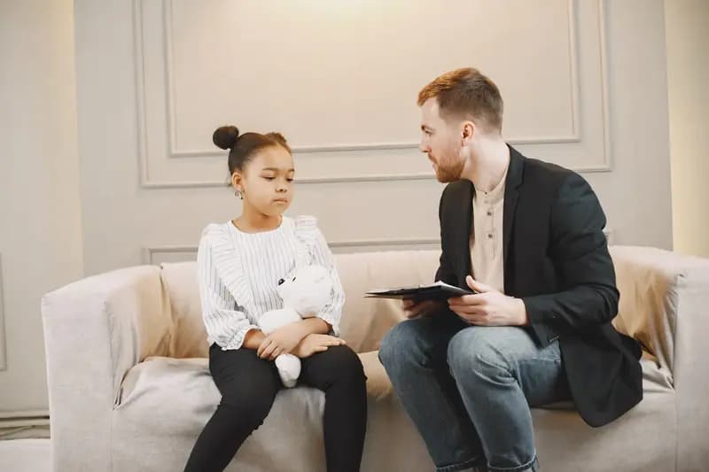 Man speaking to a sad girl holding a teddy bear