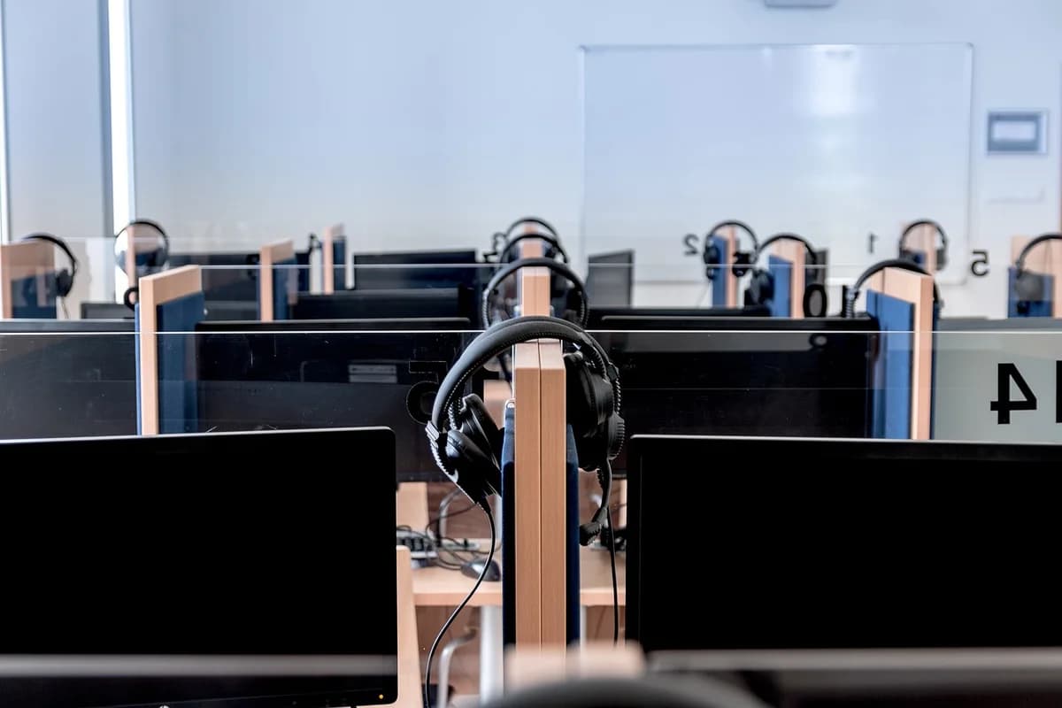 Rows of computer workstations with monitors and headsets in a classroom.