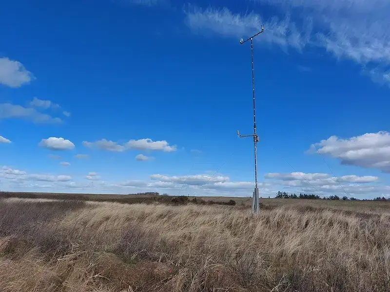Weather monitoring equipment tower in an open grassland under blue sky