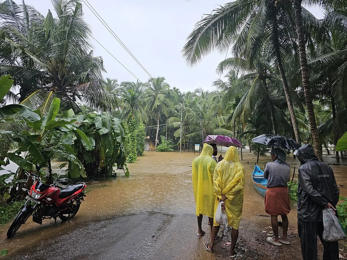 People stand on a flooded road in Kerala, India, during heavy rain.