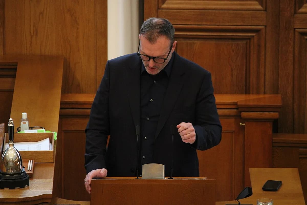A man speaking at a podium in the Danish Parliament chamber.