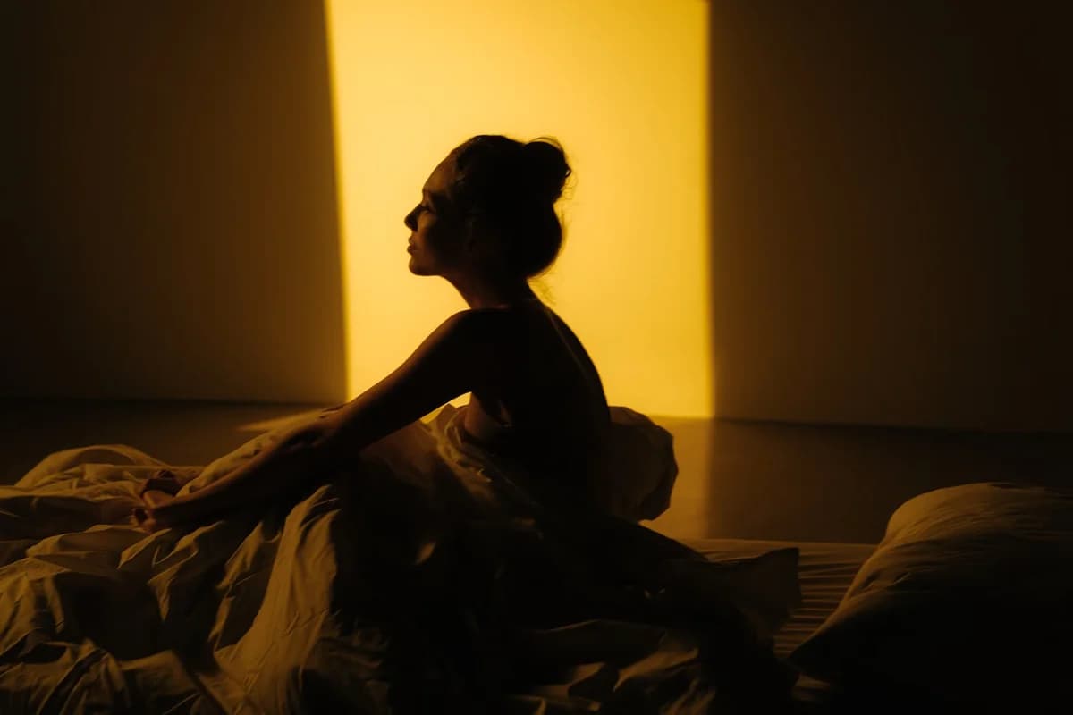 Silhouette of a woman sitting on a bed in warm sunlight.