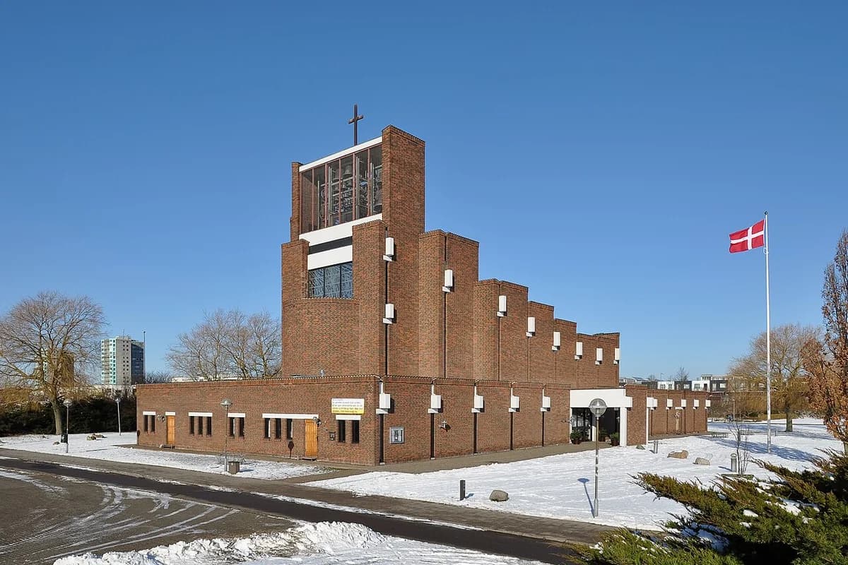 A brick church in winter with a Danish flag and a cross on the roof.
