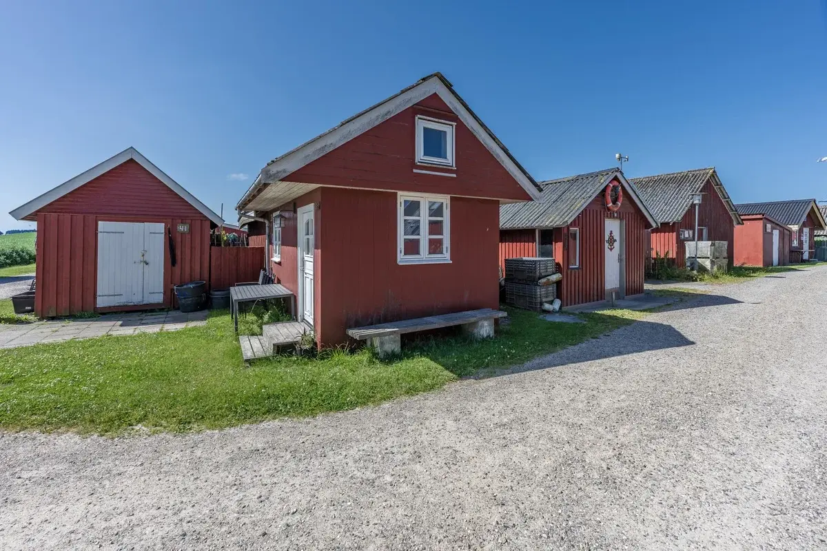 Red fishing huts beside a gravel path under a clear blue sky.