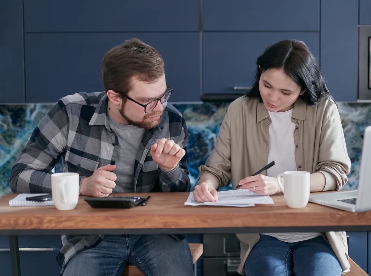 A couple reviews documents and discusses finances at a kitchen table.