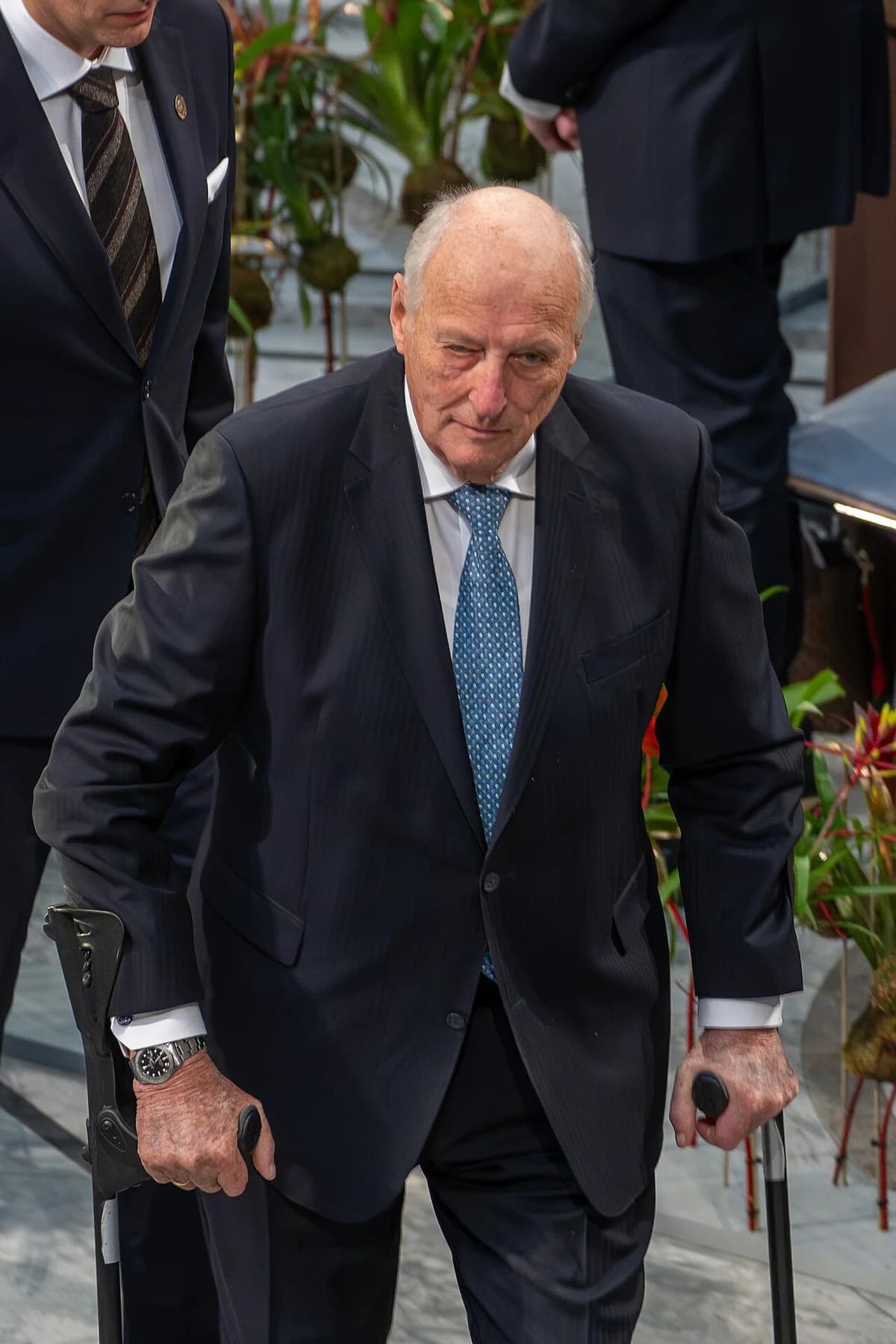 Elderly man in suit using crutches at a formal event