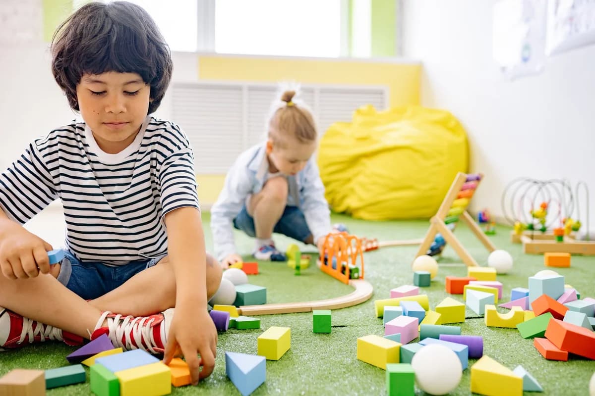 Two young children playing with colorful blocks in a bright daycare classroom.