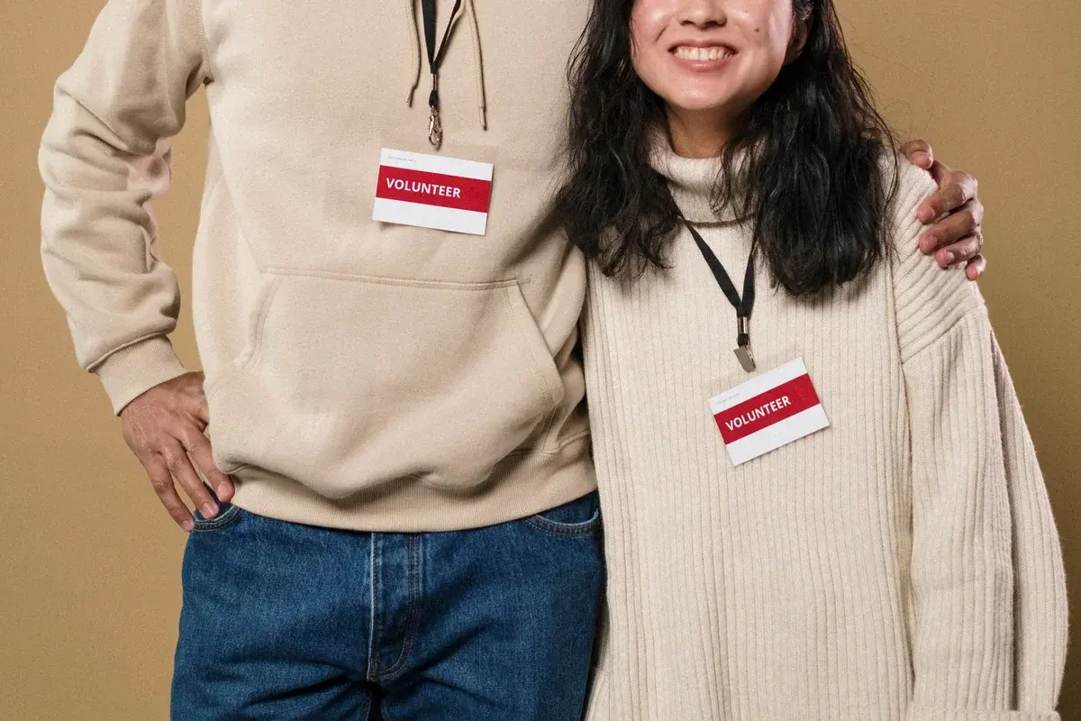 A man and woman wearing volunteer badges smile together against a beige background.