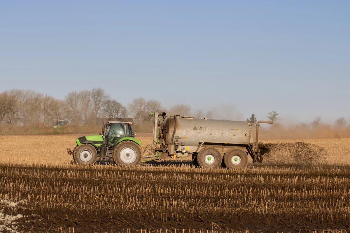 Tractor with tank trailer spreading fertilizer on a bare field