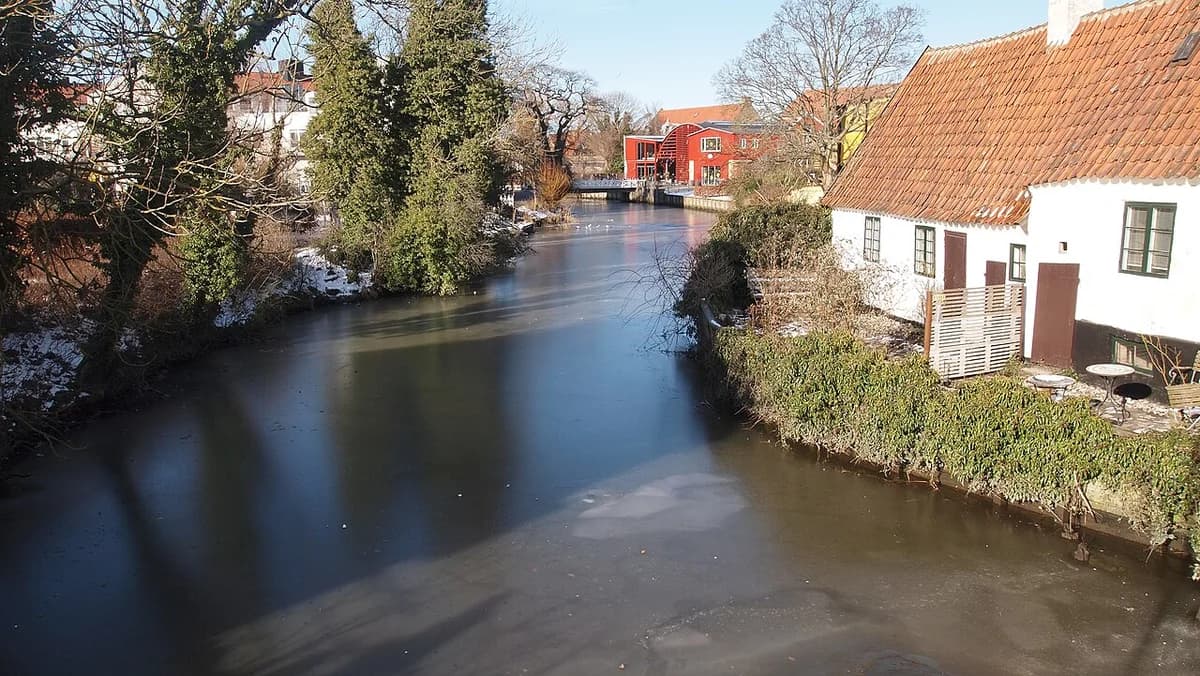 A calm river flowing past houses and trees in winter.