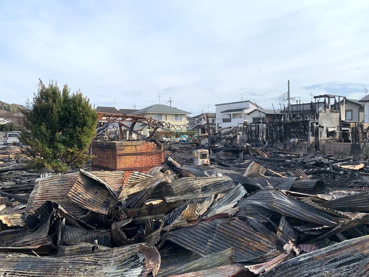 Burned-out buildings and collapsed corrugated metal after a major fire in a residential neighborhood.