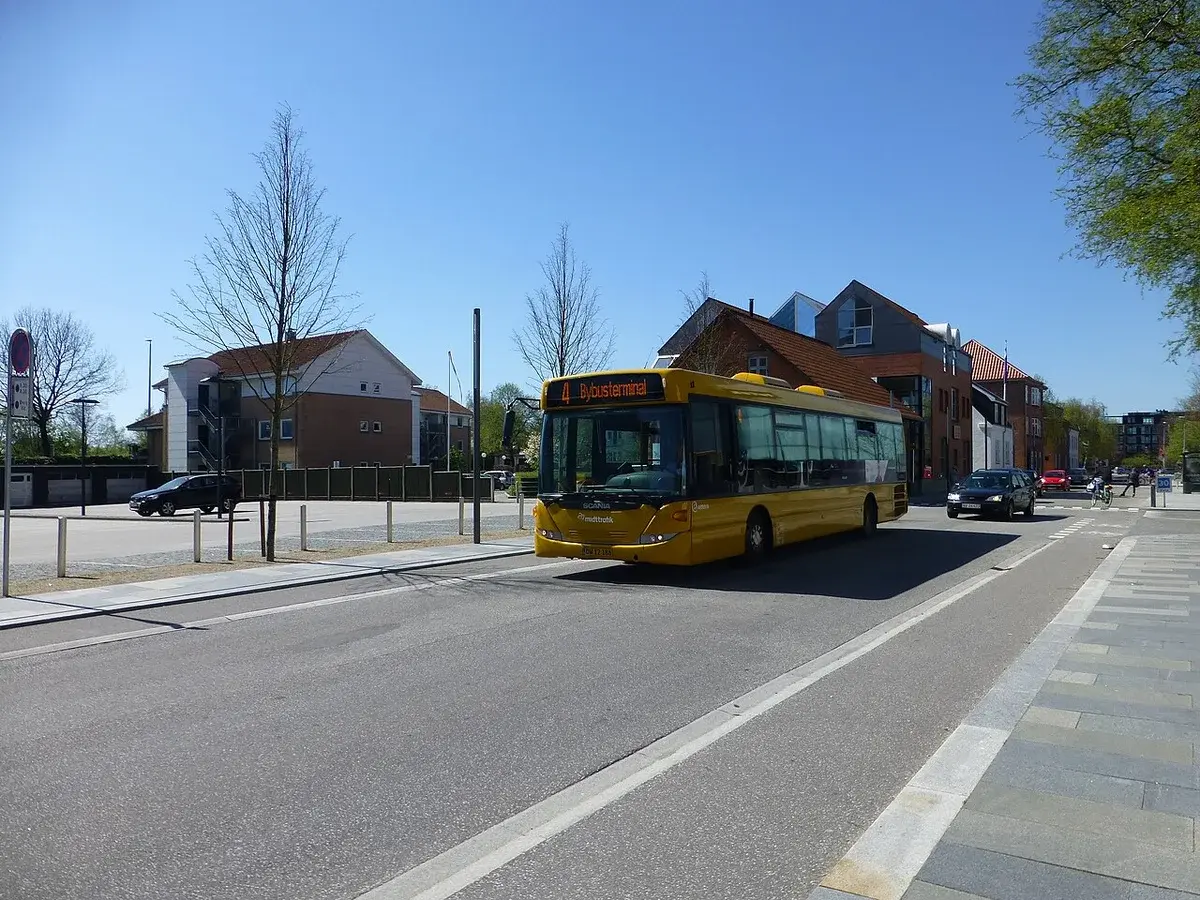 A yellow city bus driving down a street in Herning, Denmark.