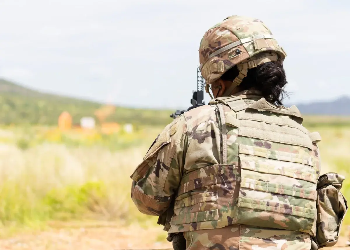 A soldier in camouflage and a ballistic vest training outdoors.