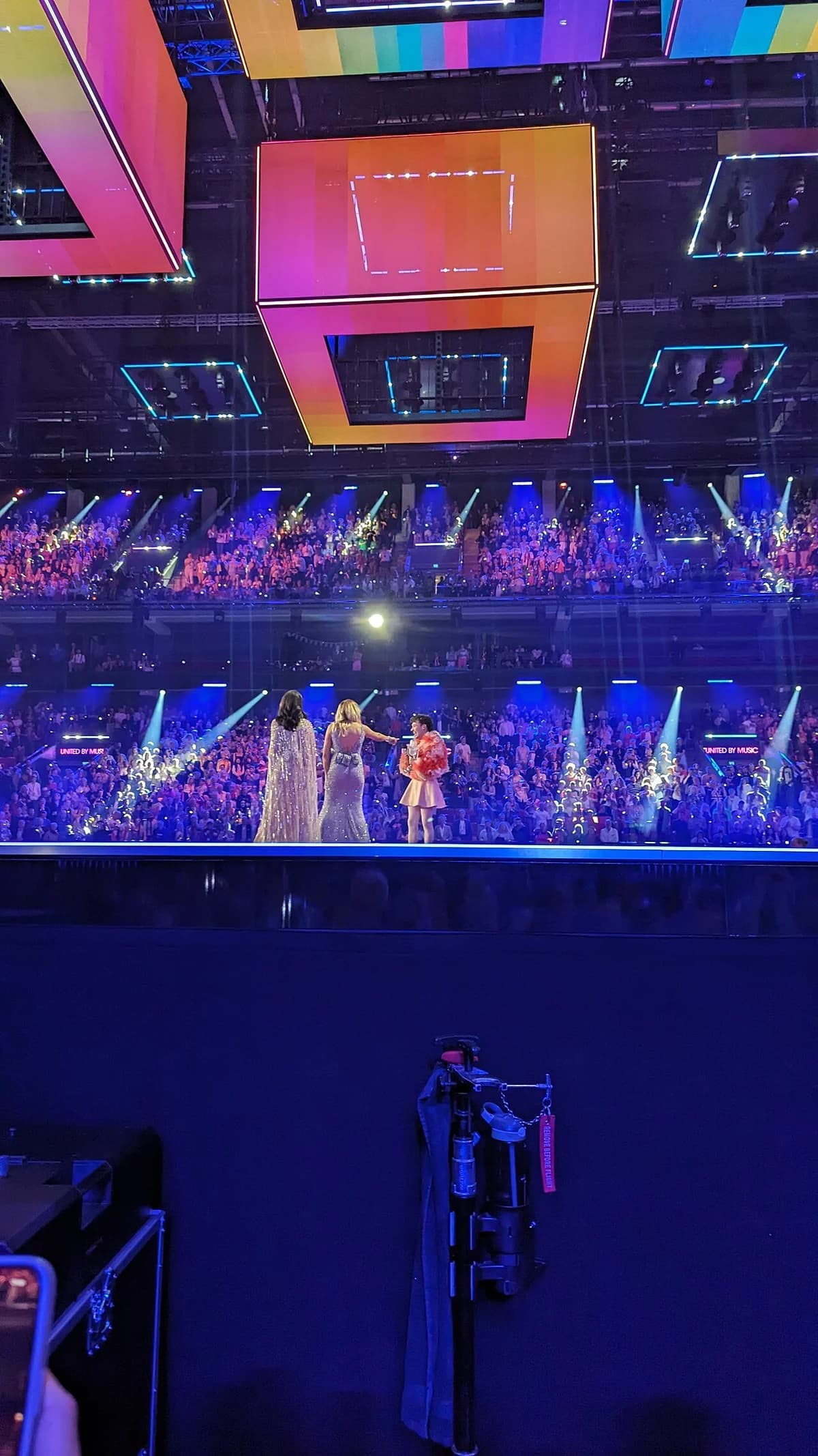 Nemo stands on stage with two hosts in a packed Eurovision arena.