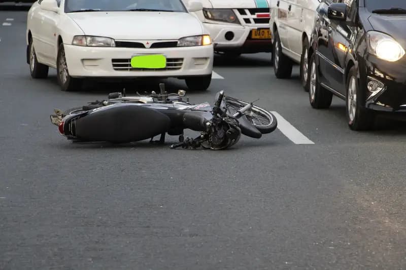 Motorcycle lying on city road among cars after accident