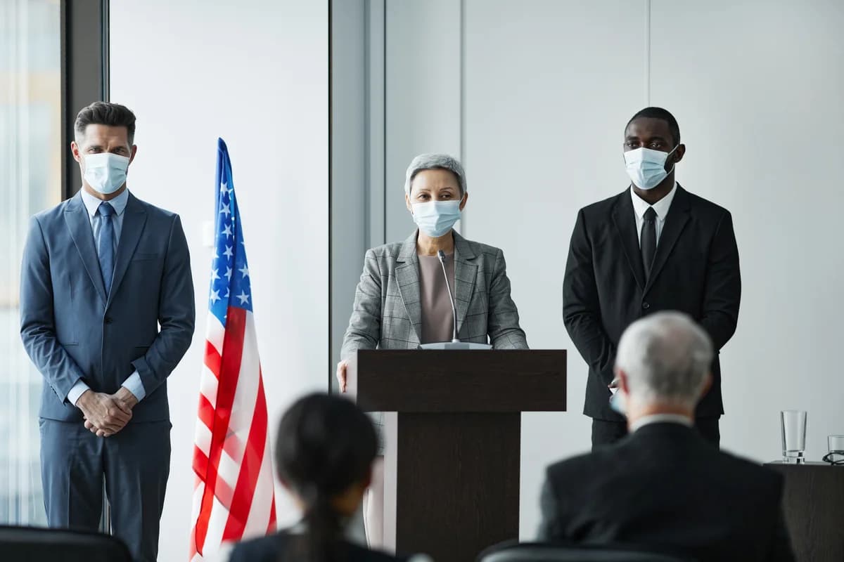 Three masked business leaders stand at a podium beside an American flag during a conference.