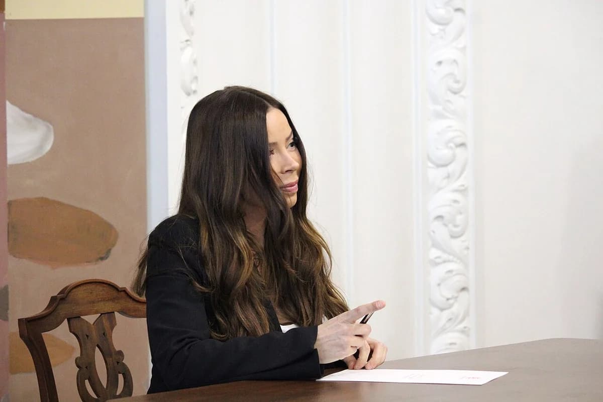 A woman signs a declaration at a table in a formal chamber.