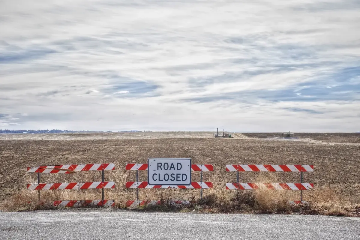 A road closed sign blocks a rural road in an open field.