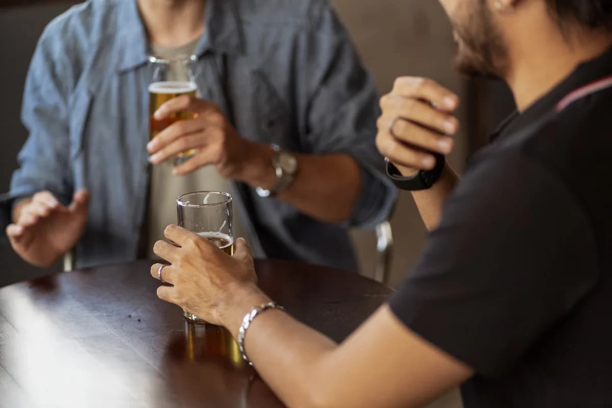 Two adults talking indoors while holding glasses of beer.