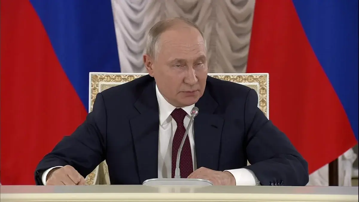 Vladimir Putin speaking at a press briefing with Russian flags behind him.