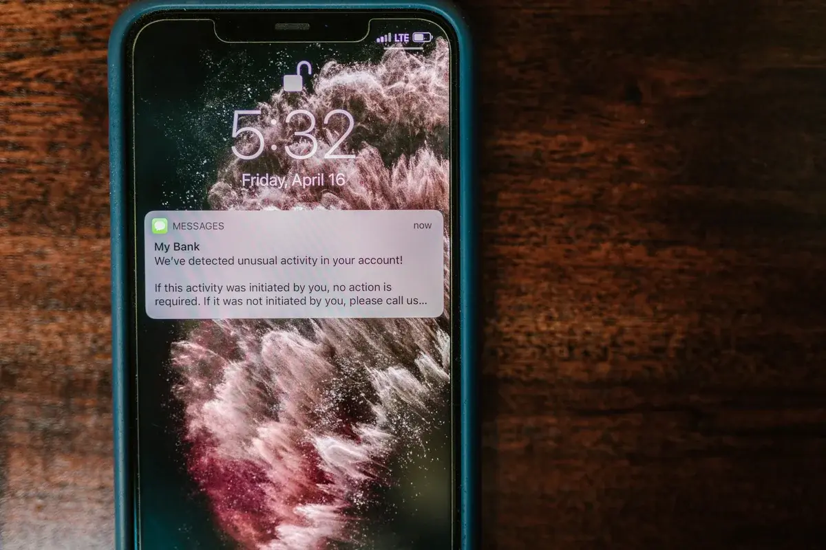 Close-up of a smartphone displaying a bank alert on a wooden table.