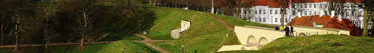 Panoramic view of grassy fortifications with a white water tower and buildings in the background.