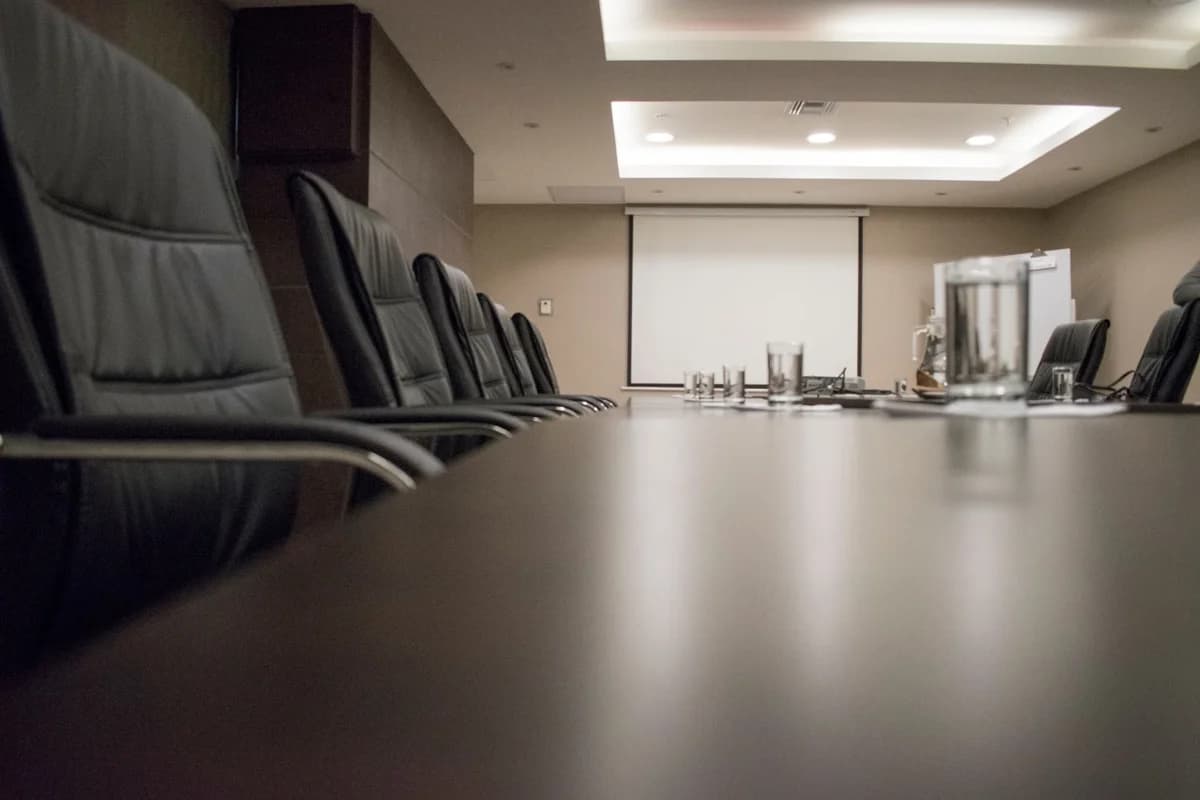 Empty conference room with black chairs, a projector screen, and glasses on a meeting table.