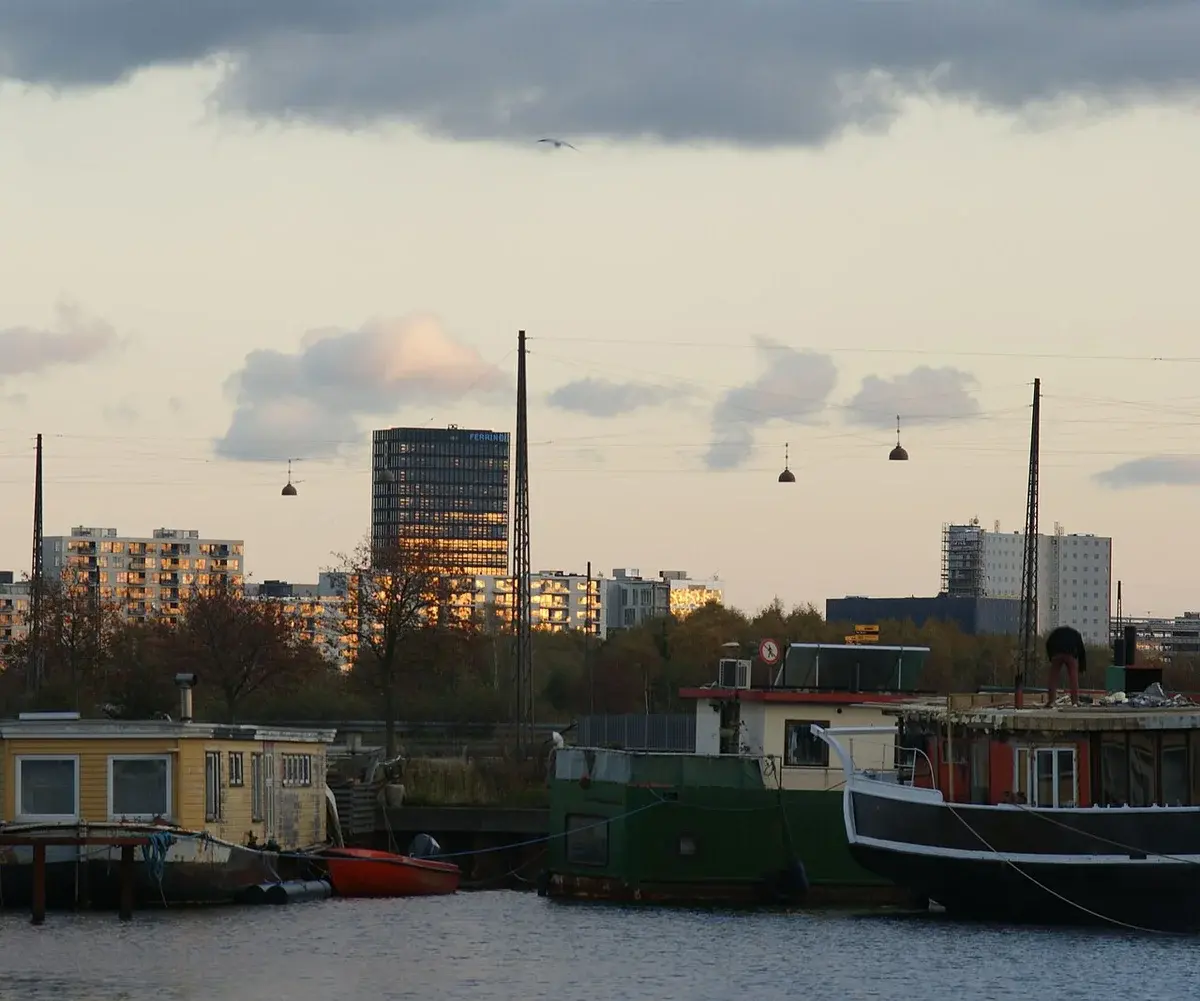 Houseboats on the water with modern buildings in Copenhagen in the background.