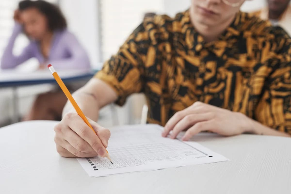 A student writes an exam with a pencil in a classroom.