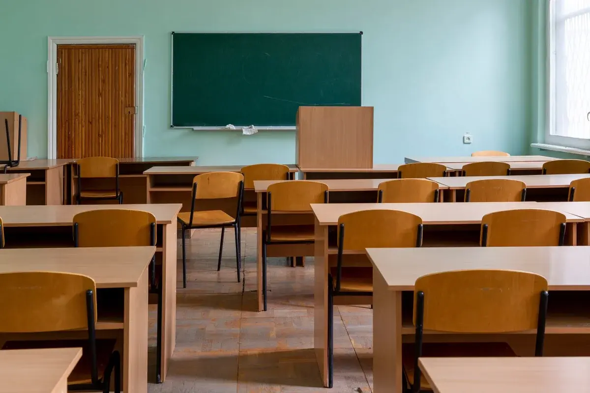 An empty classroom with wooden desks and chairs facing a green chalkboard.