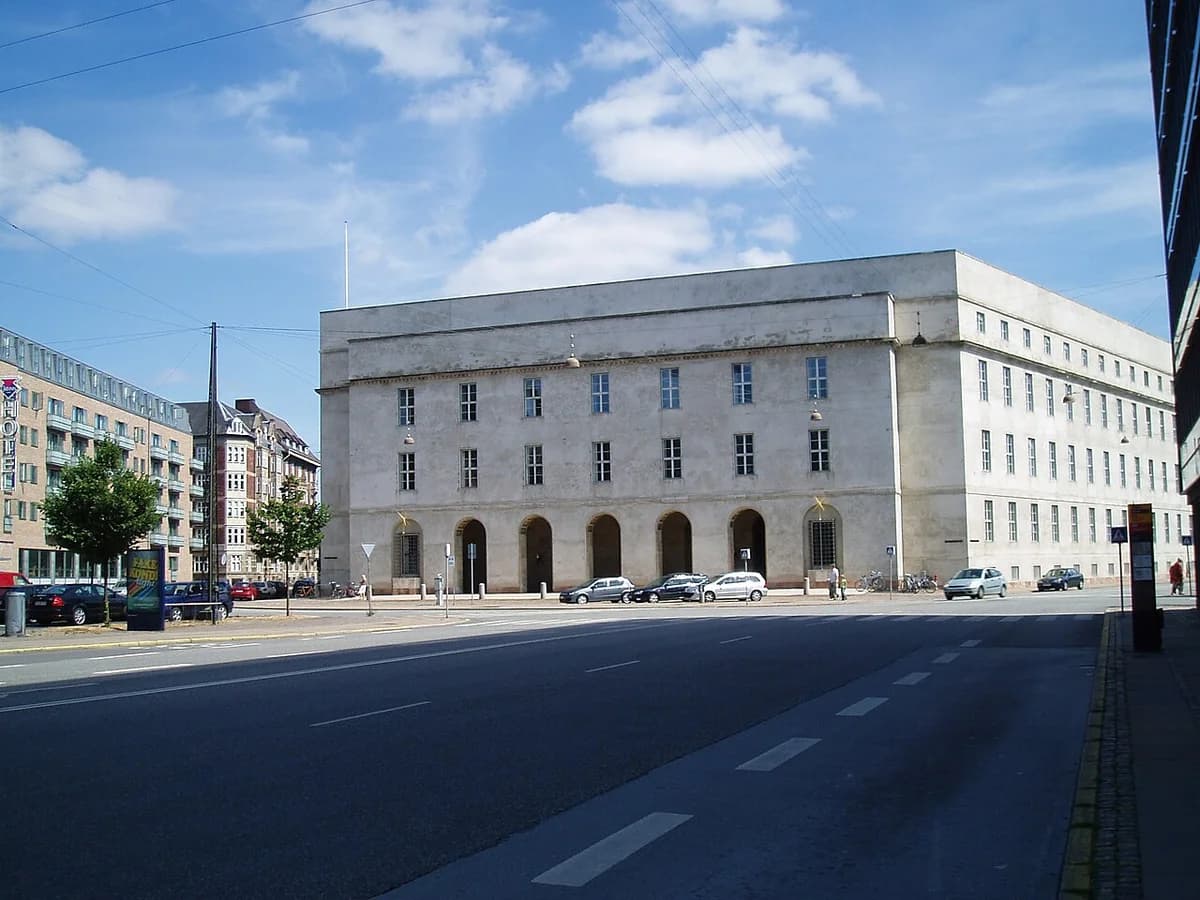Large stone police headquarters building on a Copenhagen street with parked cars.