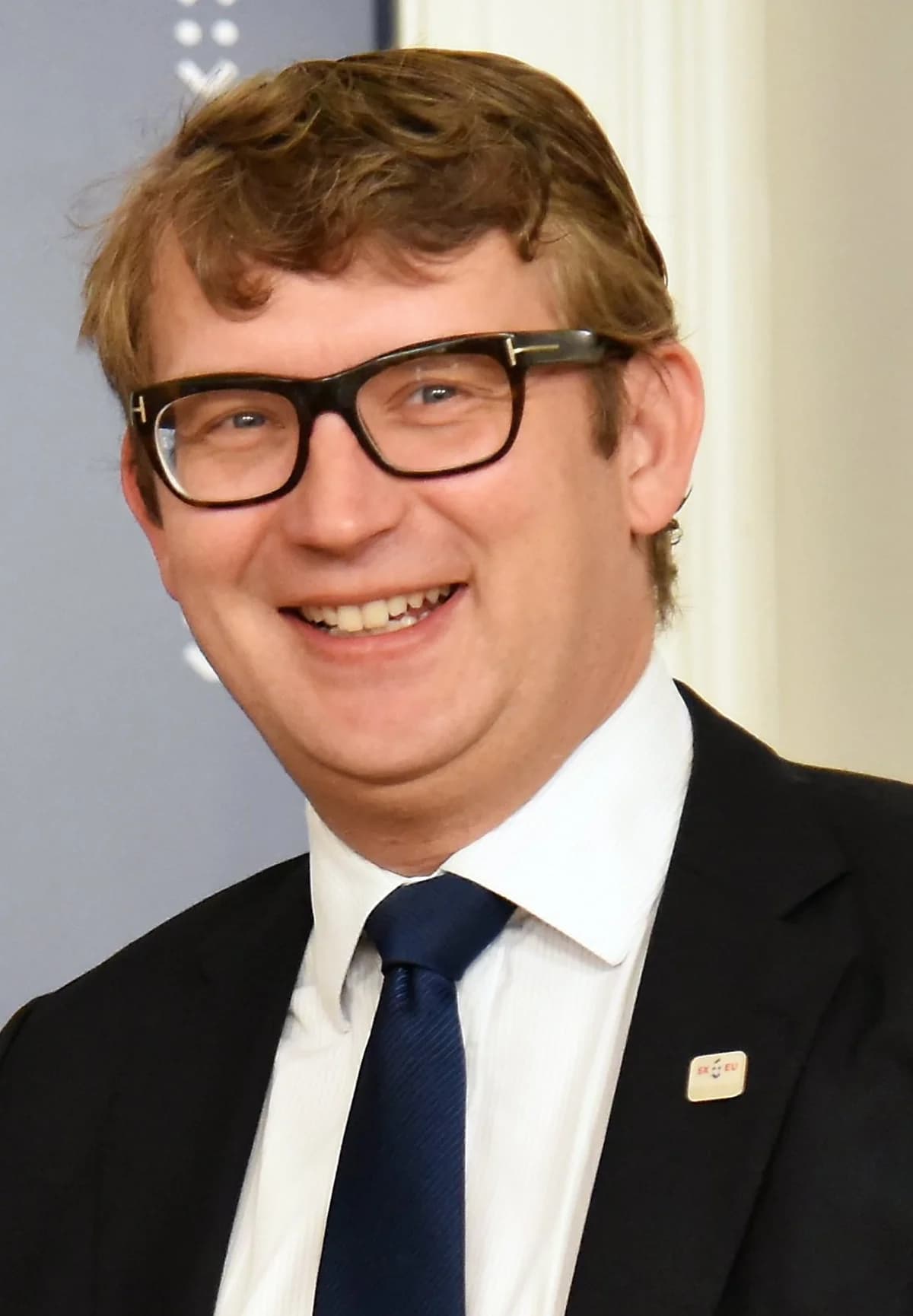 Portrait of Troels Lund Poulsen smiling in a suit and glasses.