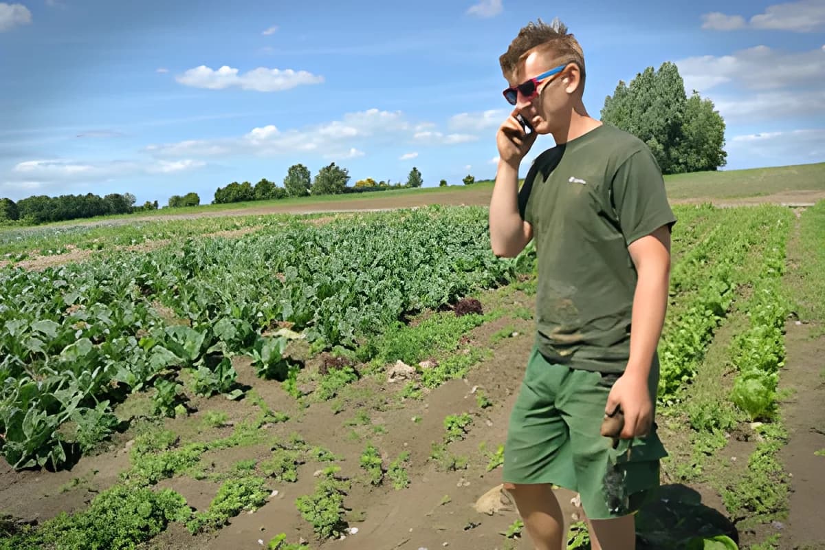 A man talks on a mobile phone while standing in a vegetable field.