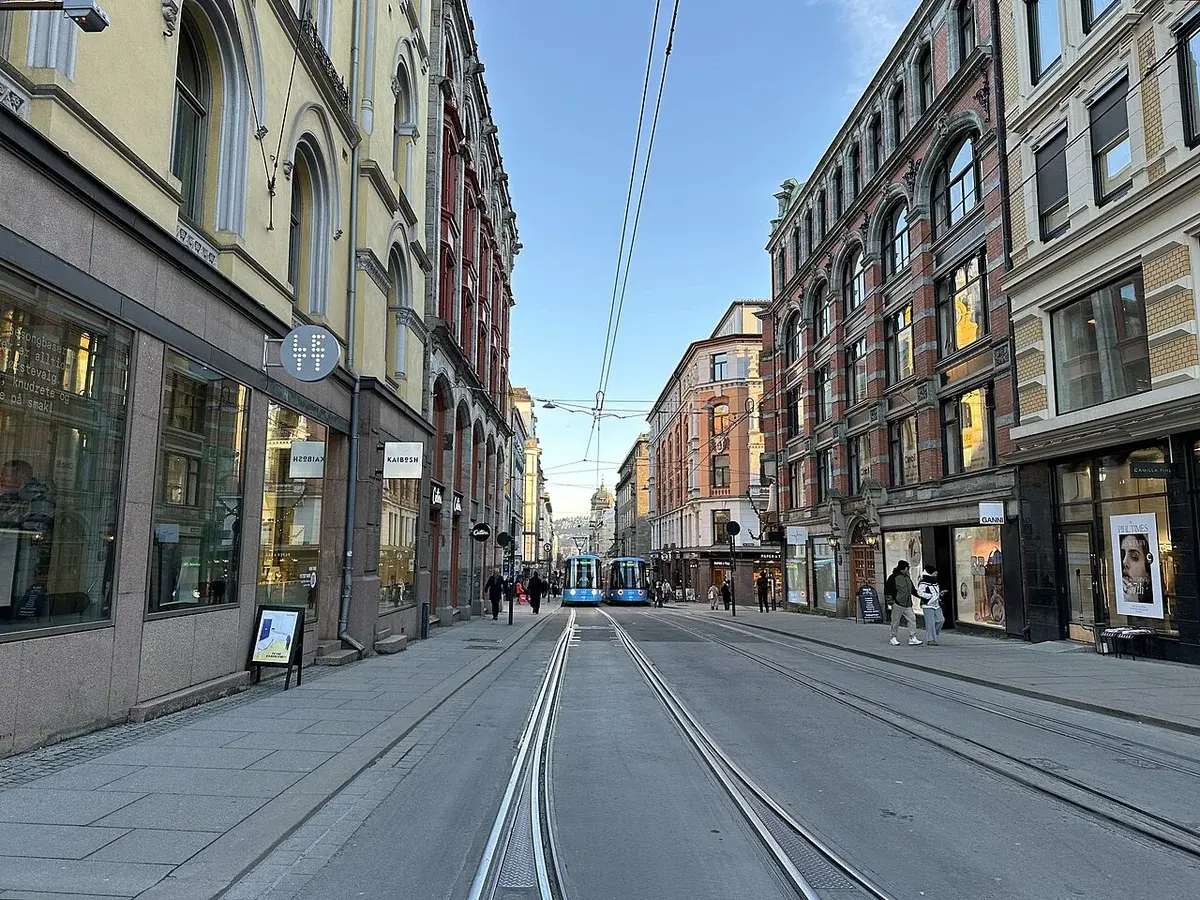 A city street in Oslo with tram tracks, historic buildings, and pedestrians.
